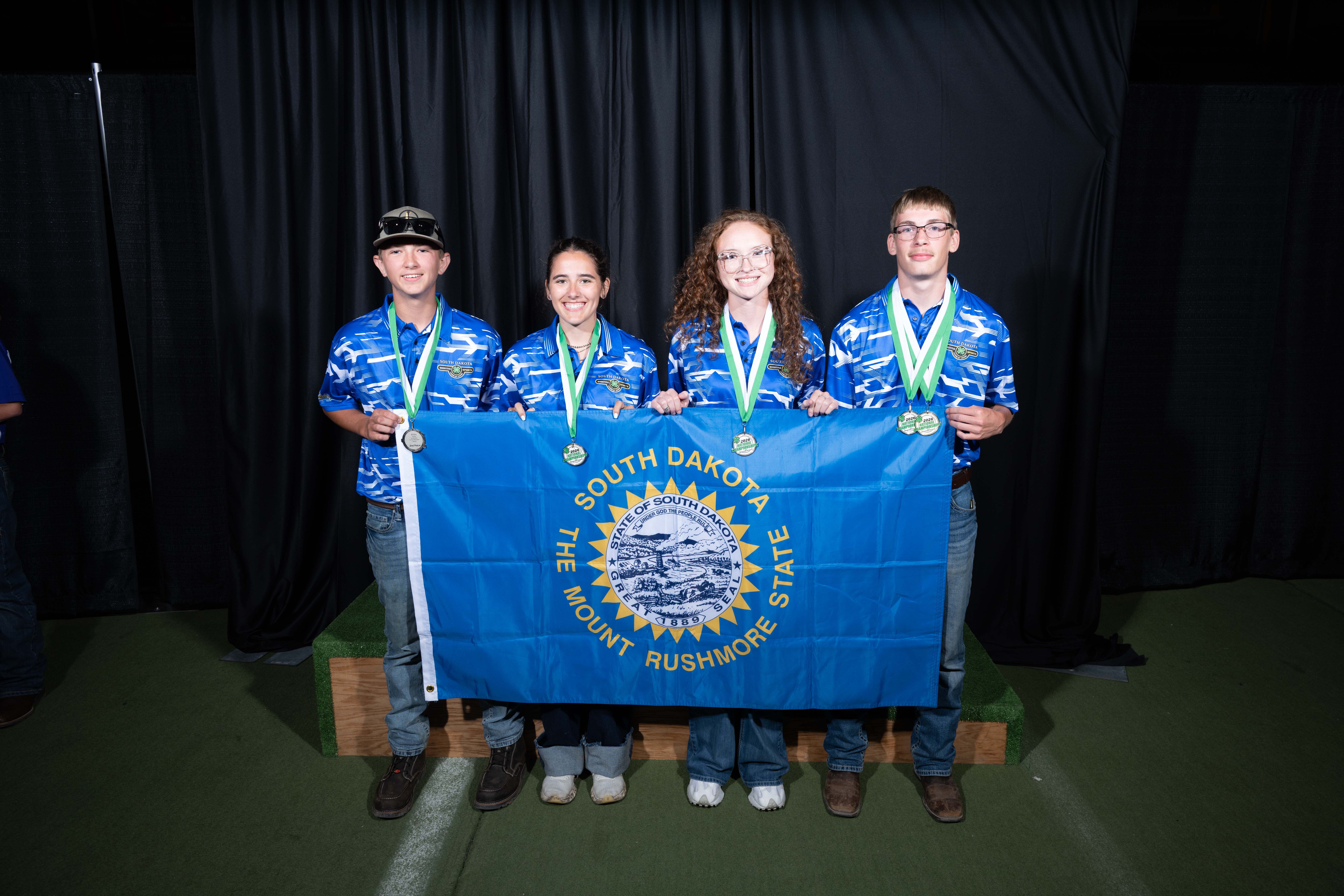 Four youth stand holding a South Dakota state flag