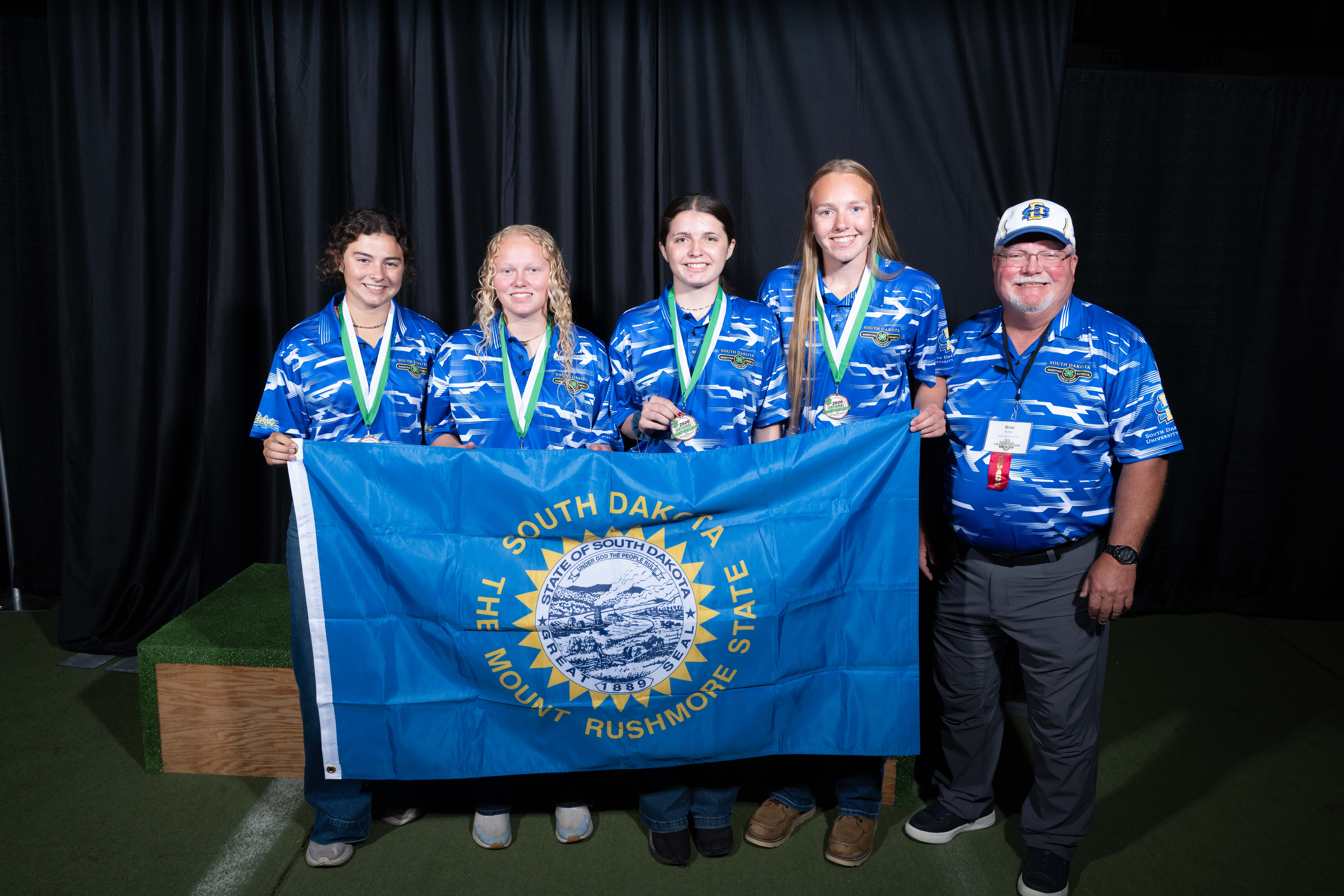 Four teenage girls and their coach hold up a South Dakota flag