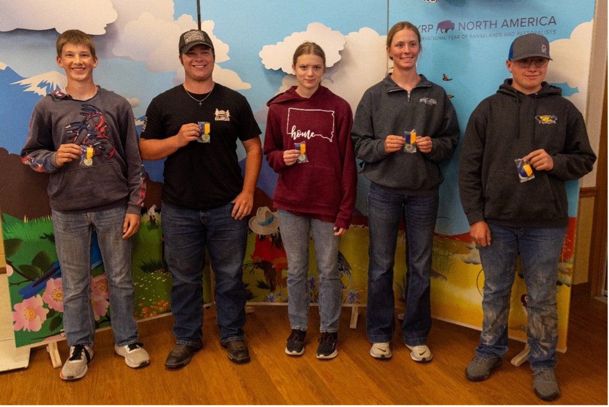 Five teenagers smile holding small medals