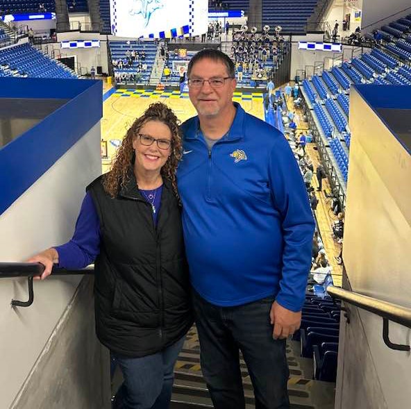 A couple smile for the camera inside a basketball stadium