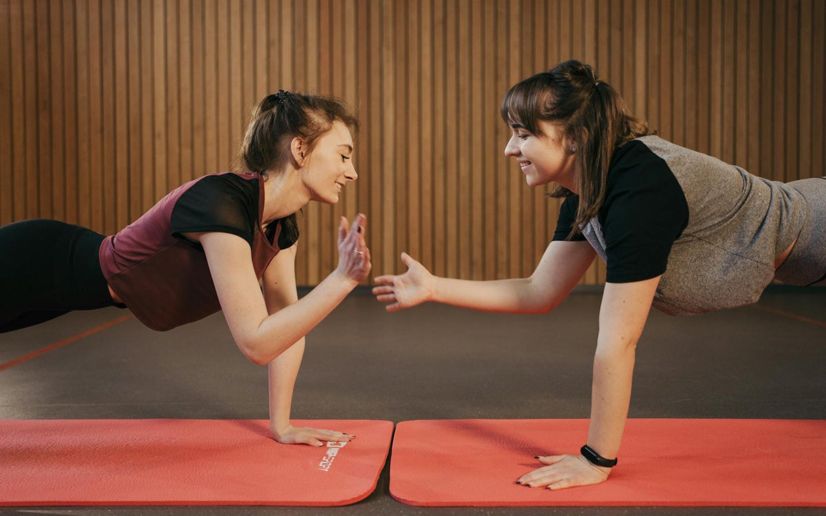 Two young women doing a plank exercise in a gym.