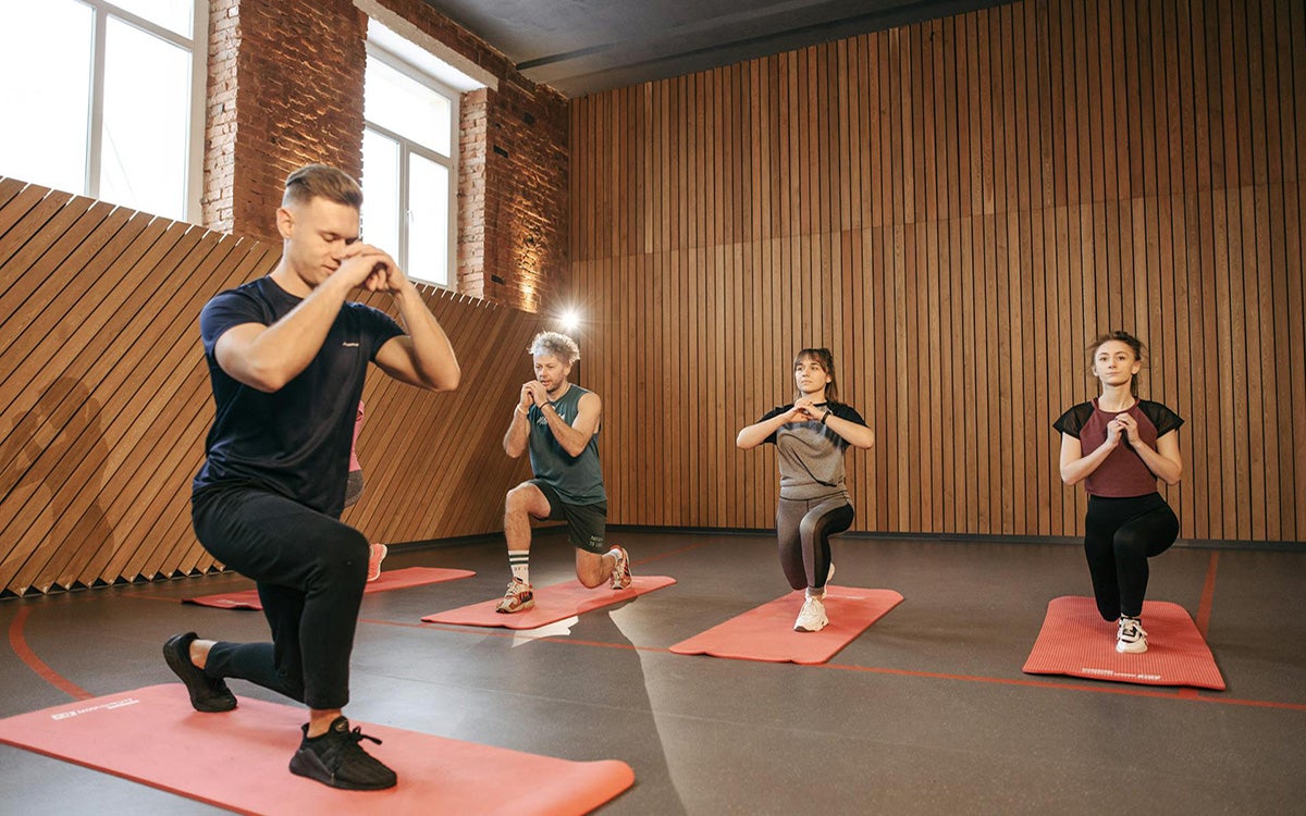 Fitness instructor leading a group of young adults in a lunge exercise.