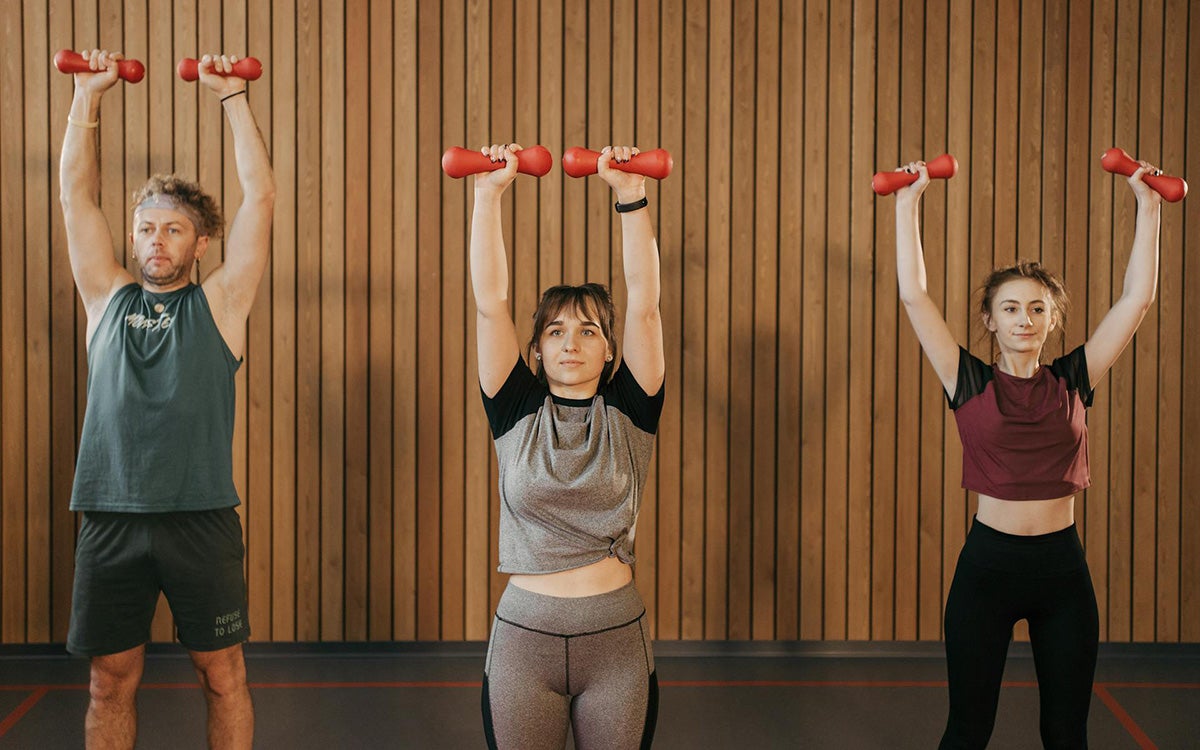 Group of young adults doing the overhead press exercise in a gym.
