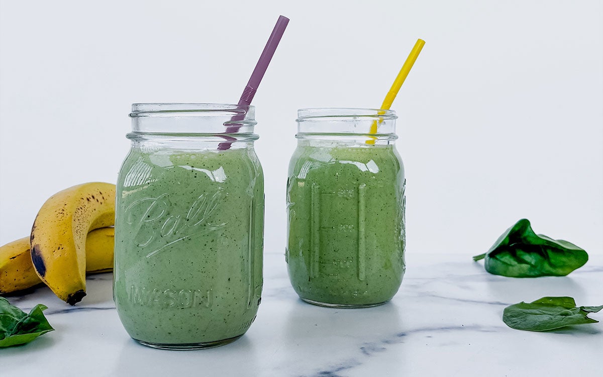 Two green smoothies in Mason jars on a countertop.