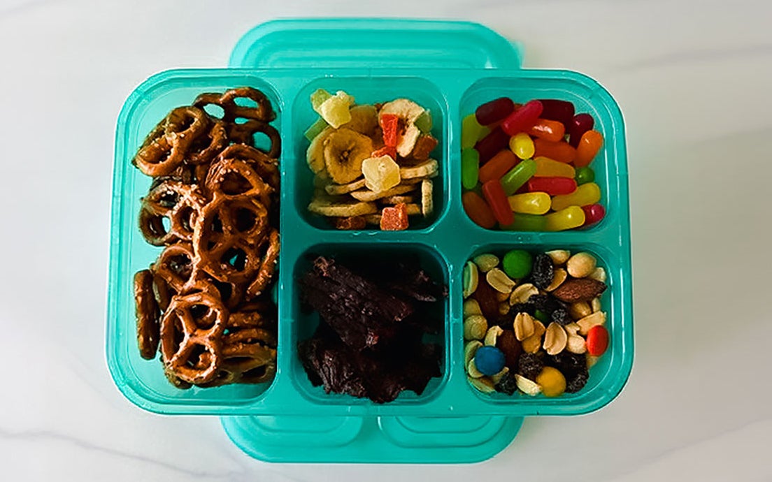 Road trip snackle box with pretzels, dried fruit, raisins, trail mix, and candy.