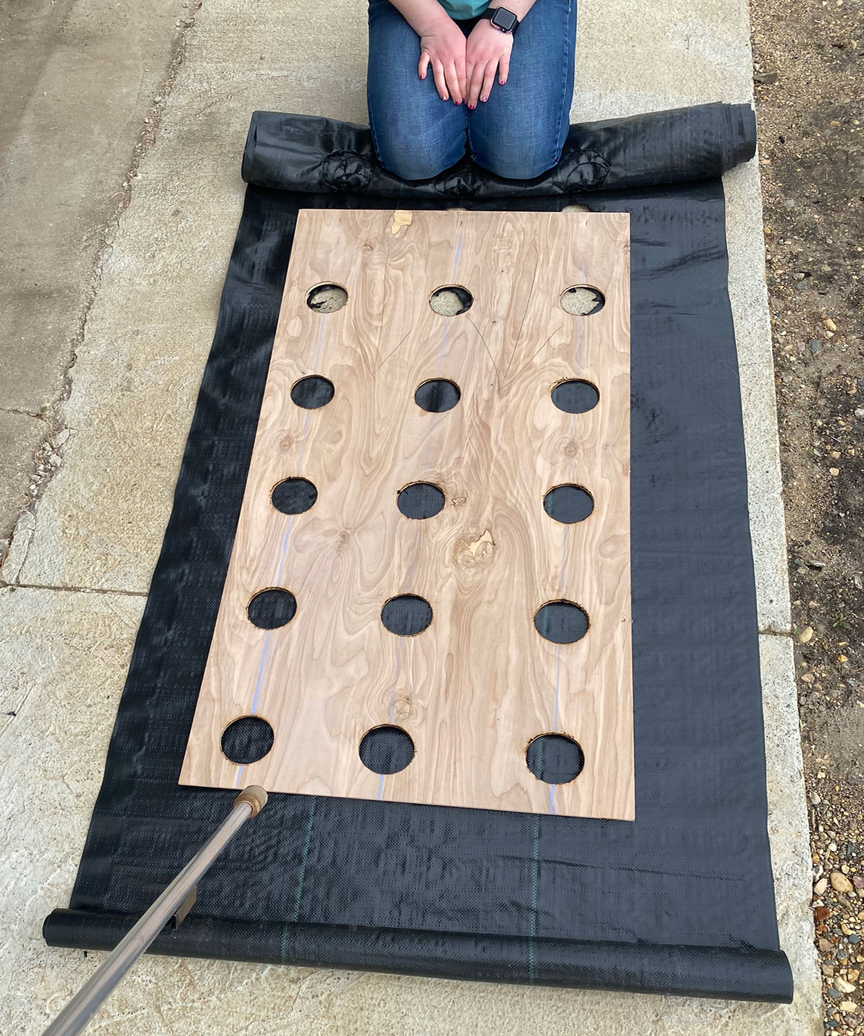 Landscape fabric with a wooden, 9 by 9-inch grid template placed on top of it.