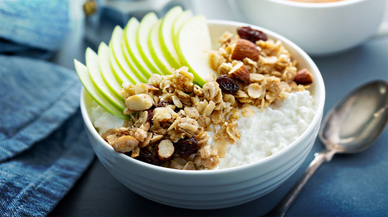 Apple slices and granola on top of a container of cottage cheese.