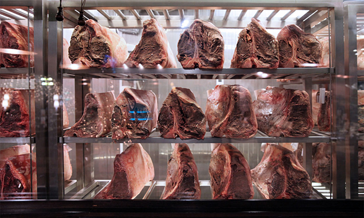 Several large cuts of beef being dry aged in a large cooler.