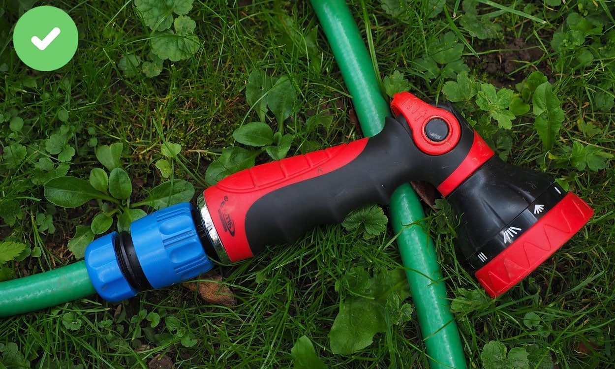 Hand holding a red, push-lever watering nozzle.