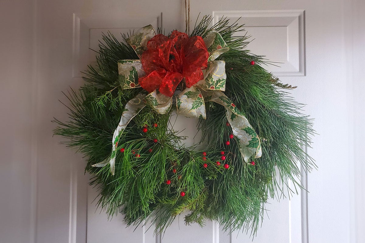 Wreath with holly and red bow hanging on a white door