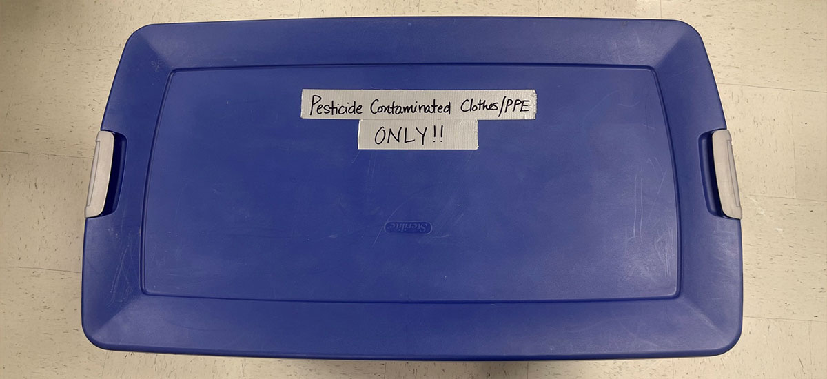 Blue container with lid visible that has a label indicating it is only for pesticide contaminated clothing/PPE.