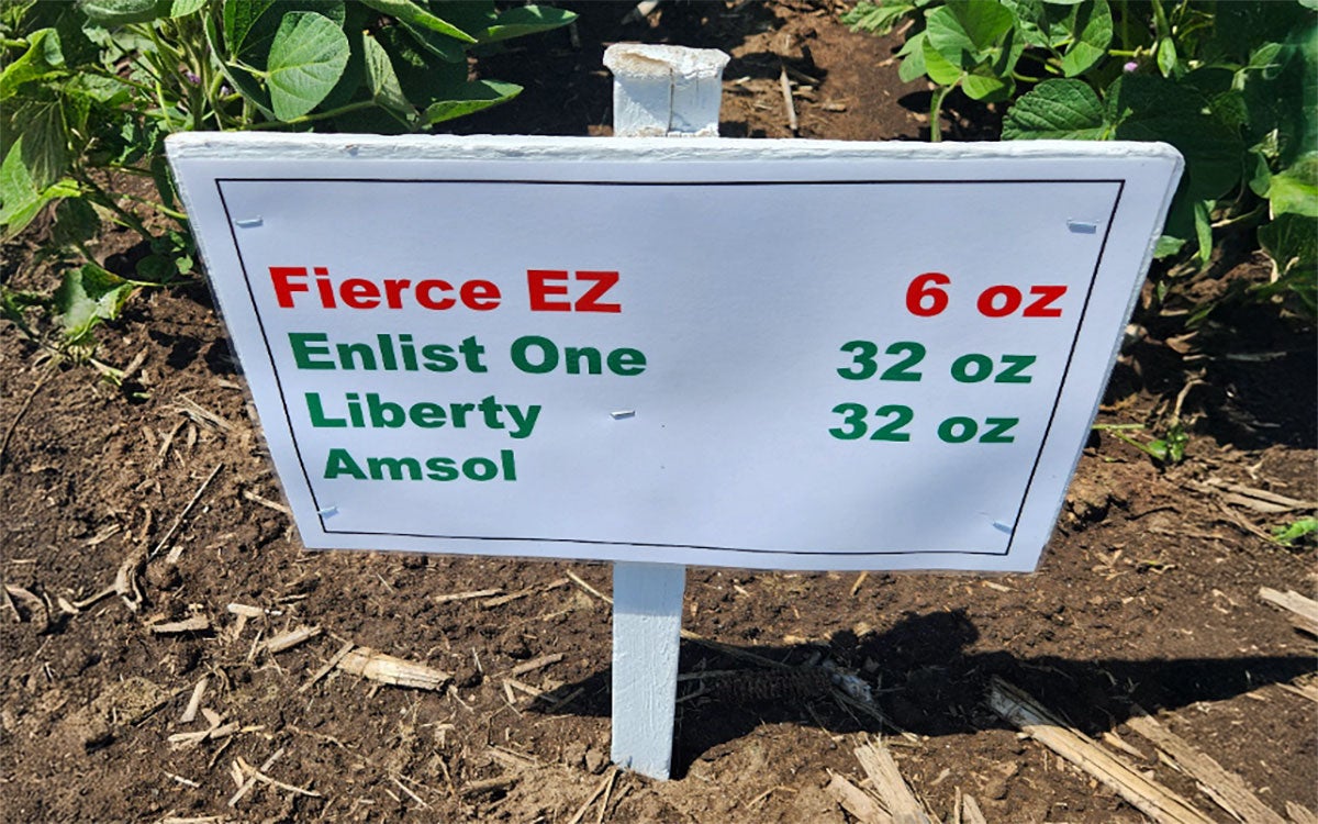Small white sign with red and green letters throughout describing what chemicals were applied on the green soybeans behind.