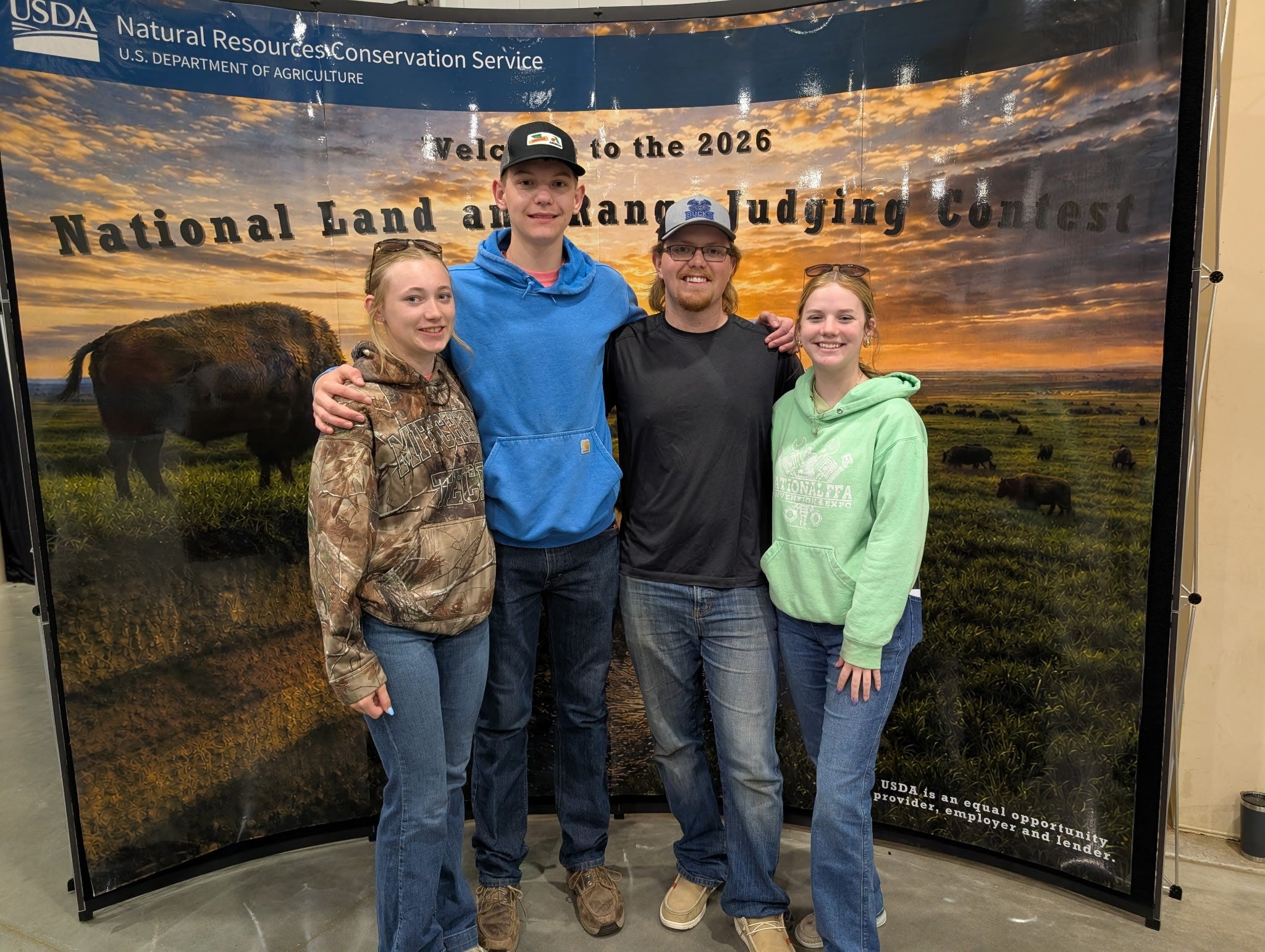 Four youth smile in front of a National Land and Range Judging Contest photo backdrop