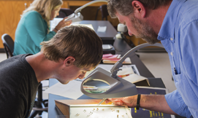 Teen boy and adult male reviewing specimens under magnifying glass.