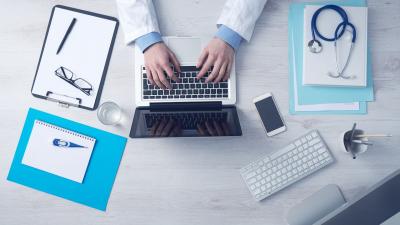 Doctor at laptop with insurance paperwork.