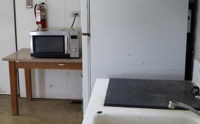 silver and black microwave sitting on a brown table next to a white fridge and a sink.