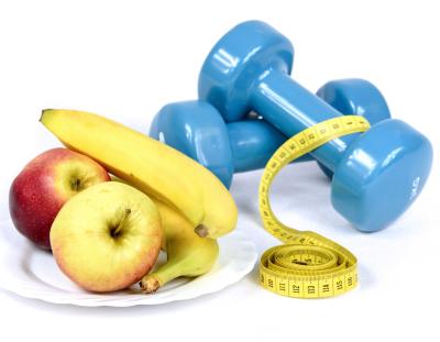 apples and bananas sitting on a plate next to a set of blue hand weights and a body measuring tape