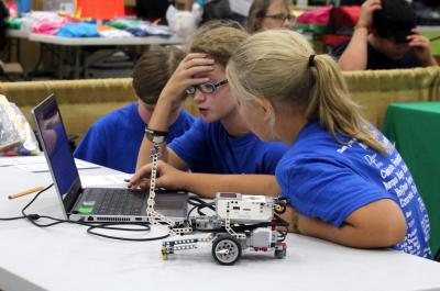 two male and one female 4-H youth inspecting a robotics control program on a laptop