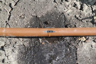 copper colored hose with a small hole in the middle. water is dripping from the hole.