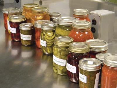 Variety of home-canned, pickled vegetables on a silver table in a kitchen.