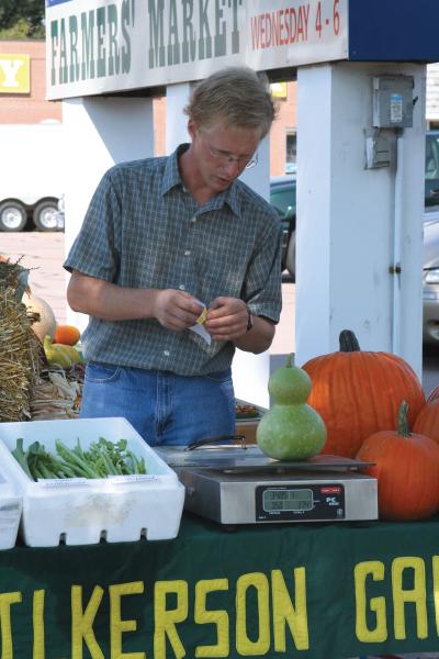 Male merchant weighing a green gourd on a digital scale at a farmers market.