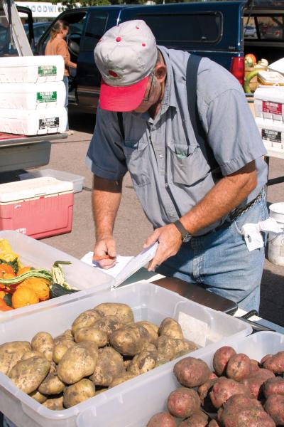 And older male vendor logging sales in a ledger at a farmers market stall.