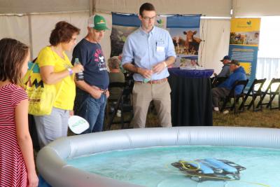 John McMaine, Assistant Professor & SDSU Extension Water Management Engineer, demonstrating an underwater drone in a large pool to a young woman and an older couple.