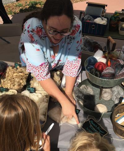 Woman demonstrating different types of wool to two children.