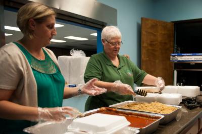 Two women preparing take-out containers for drive-up meal service.