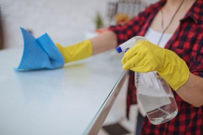 A woman wearing yellow, rubber gloves, spraying a homemade bleach solution on a kitchen counter.
