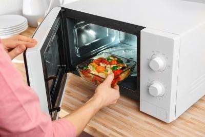 Woman putting bowl with vegetables in microwave oven.