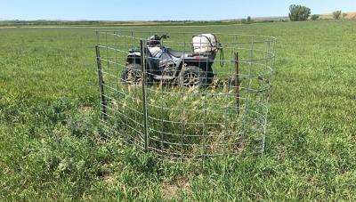 A 4-wheeler parked beside a wire cage enclosure around smooth brome and Kentucky bluegrass on grazing land.