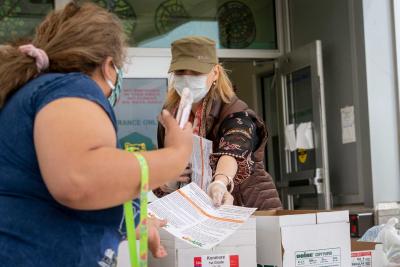 A local official wearing a mask handing a set of instructions to a woman also wearing a mask.