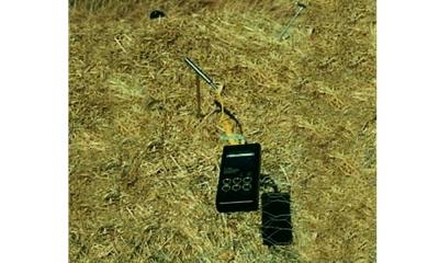 Stainless steel thermometer attached to a digital reader on a compost pile.