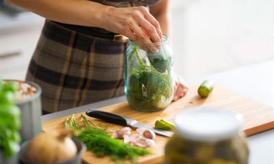 A woman preparing a jar of pickled cucumbers in a kitchen.