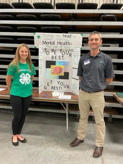 4-H member Olivia Miller standing with South Dakota 4-H Program Director Tim Tanner in front of her mental health presentation.