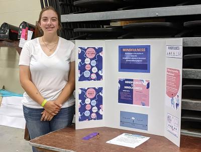 4-H member Allison Fischer standing next to her mental health presentation.