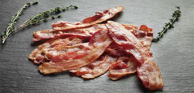 Cooked slices of bacon on a slate with fresh herbs.