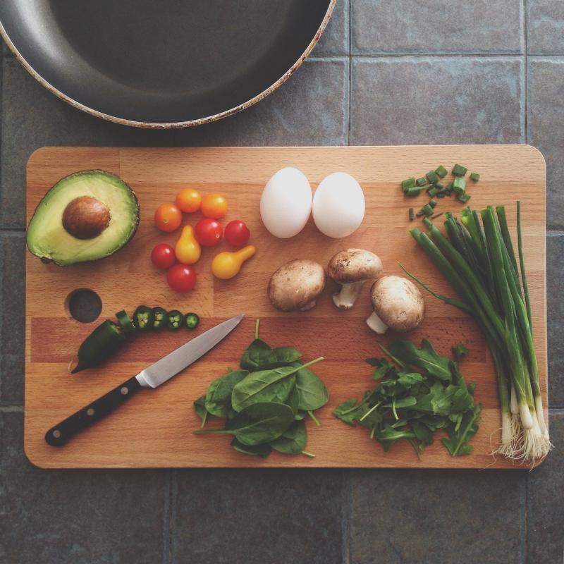 a wooden cutting board, a knife, and a frying pan with a variety of vegetables