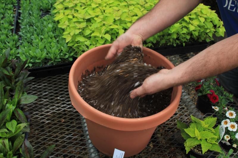 A pair of hands mixing potting soil in a brown container.