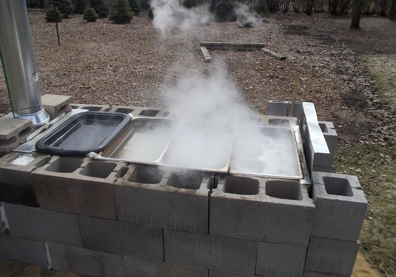 gray cinder blocks surrounding a fire. several pans of sap are sitting atop the blocks.