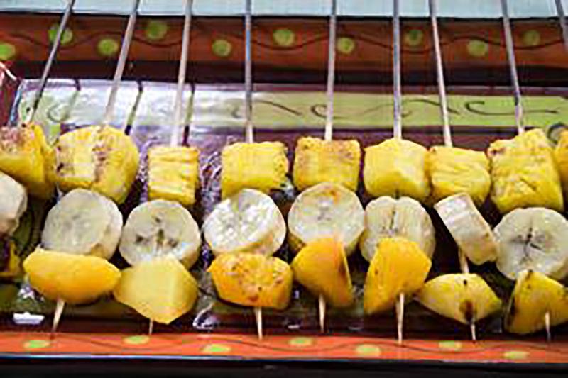 A row of fruit kabobs with pineapple chunks, banana pieces, and peach chunks ready for grilling.