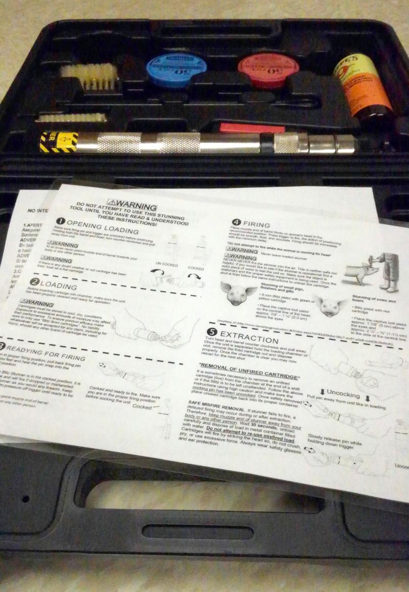 A black, plastic case containing a captive bolt stunner kit along with laminated instructions for properly using the tool for euthanasia.