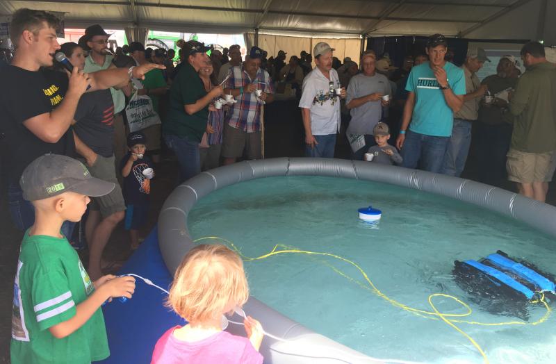 A young boy operating an underwater drone in large pool in front of a crowd of onlookers.