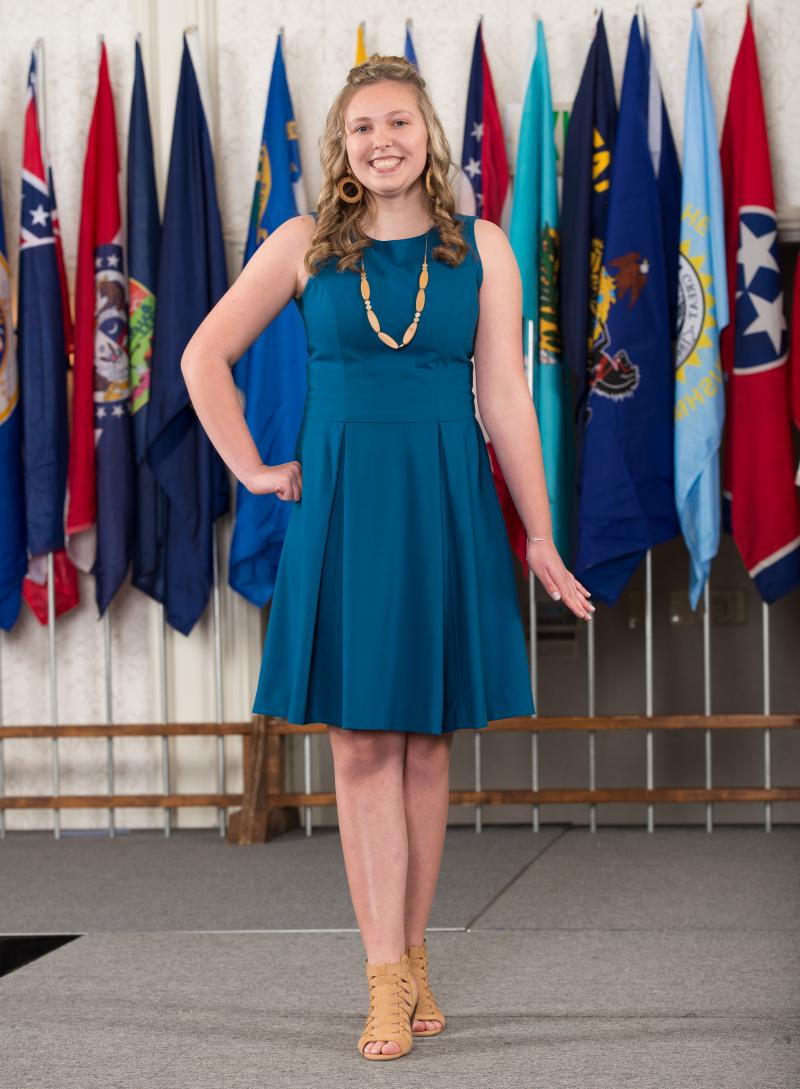 a young woman in a blue dress posing in front of a row of flags
