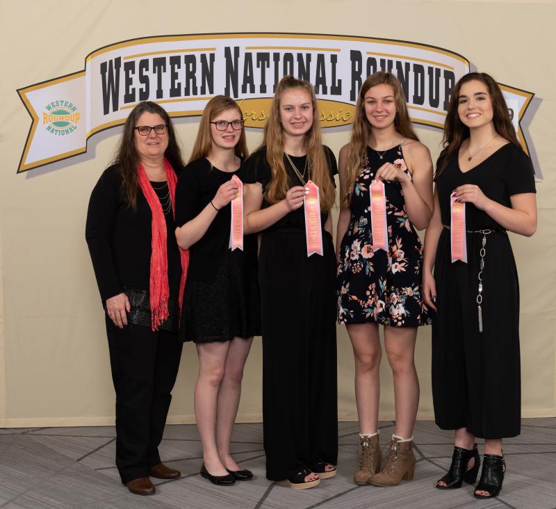 4 young women and their coach standing in front of a sign with their awards