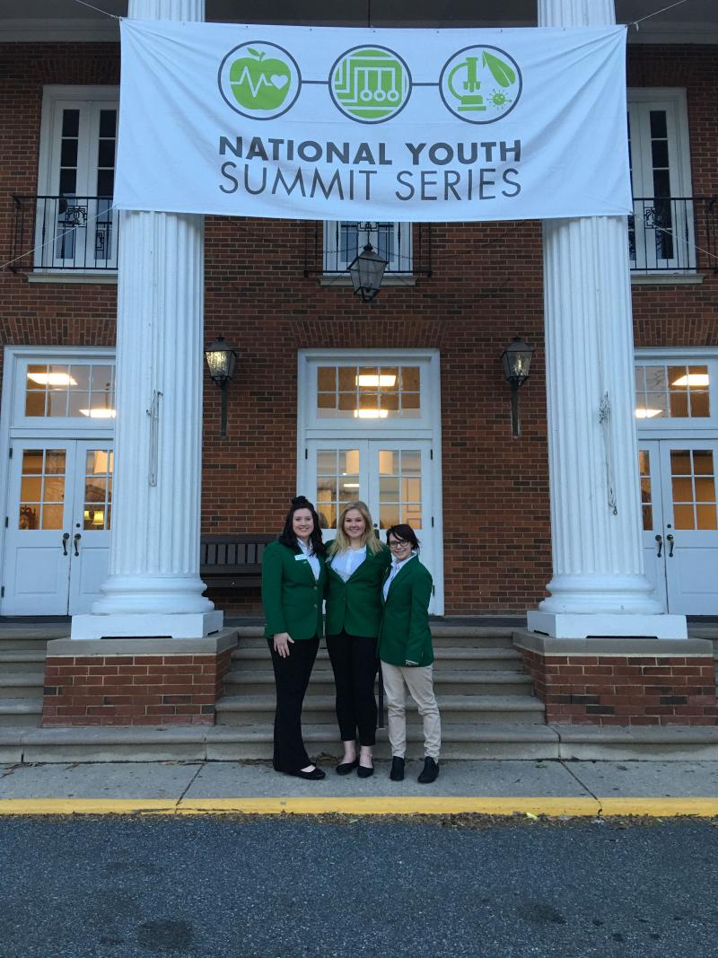 Three women in green jackets standing in front of a building