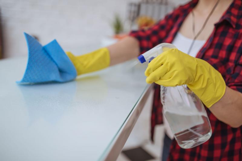 A woman wearing yellow, rubber gloves, spraying a homemade bleach solution on a kitchen counter.