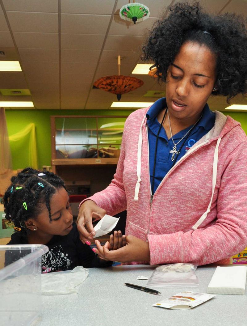 Teacher pouring a small amount of seed into a student's hand to construct a tiny greenhouse.