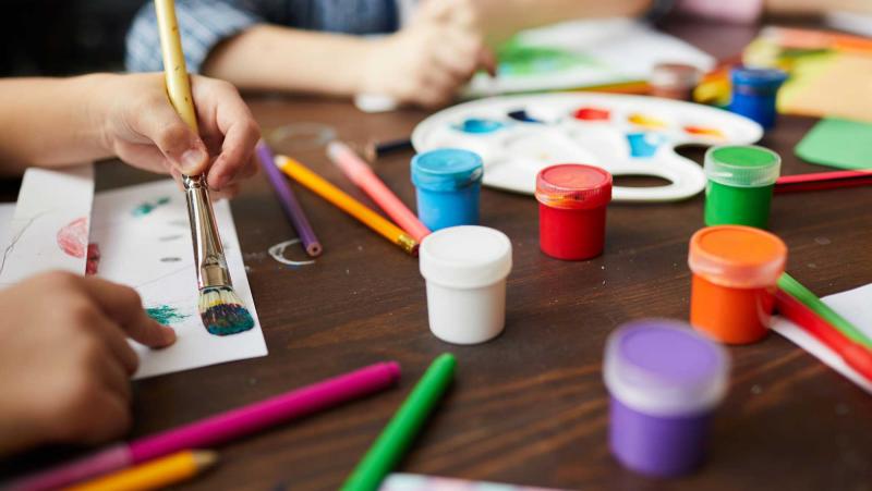 Children painting pieces of paper at a craft table.